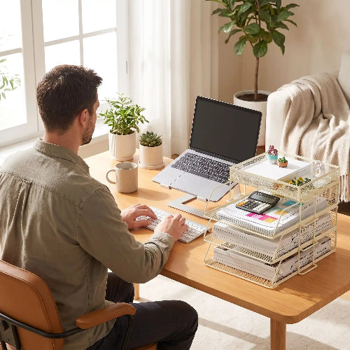 Homme assis dans son bureau dns salon travail sur son pc avec organisateur de bureau blanc posé sur le bureau 