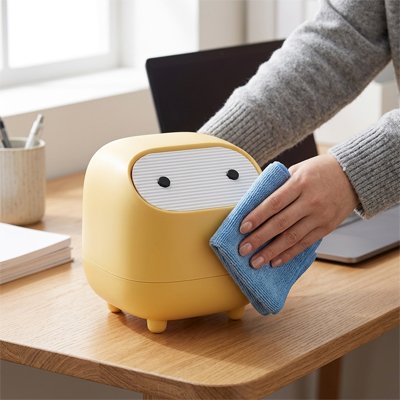 Une main netoie Poubelle de bureau jaune posée sur table de bureau